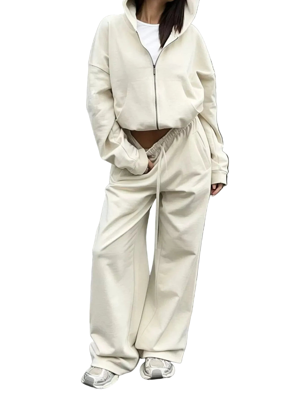 A person wearing a matching cream-colored two-piece lounge set consisting of a cropped zip-up hoodie and wide-leg sweatpants, paired with white sneakers, standing in front of a modern glass door.