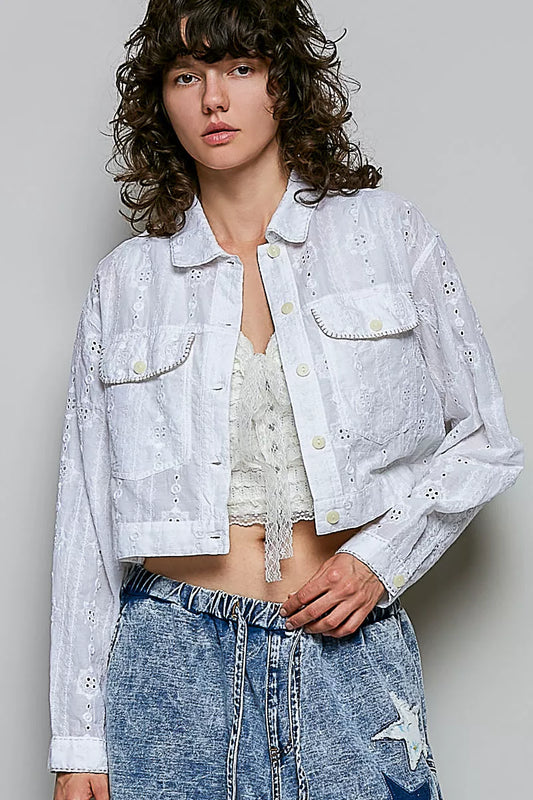 Person wearing a white embroidered jacket and blue jeans against a plain background