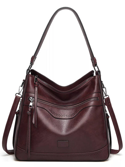 A dark burgundy leather hobo shoulder bag with multiple zippered pockets, a front pebbled panel, and a long shoulder strap, shown on a plain white background.