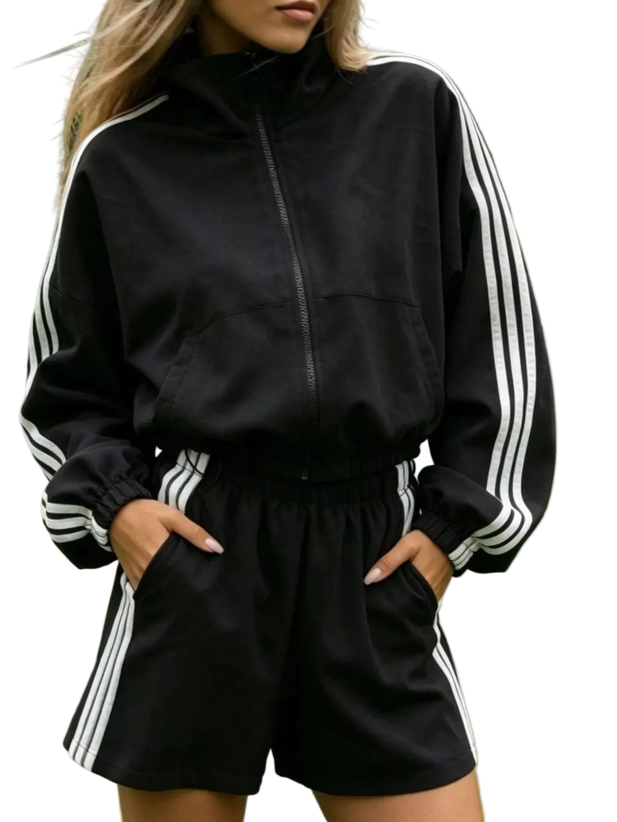 A woman wearing a black athletic tracksuit with white three-stripes on the sleeves and shorts, standing on a green tennis court.