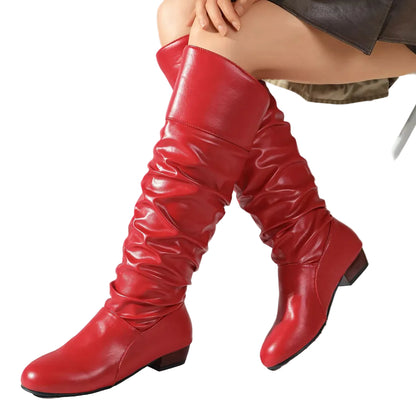 A pair of knee-high red slouchy boots with a smooth faux-leather finish, shown on a model's legs against a light gray studio background.