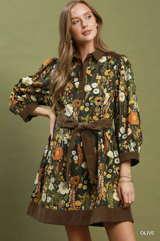 Woman wearing a floral dress with a brown belt against an olive green background