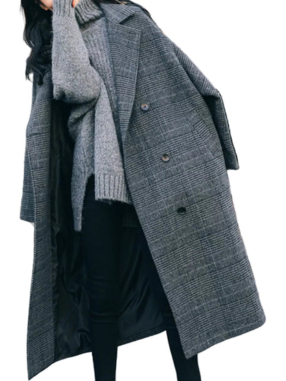 A woman wearing a long gray plaid overcoat over a black dress and gray knit sweater, standing outdoors on a paved street with urban background elements.