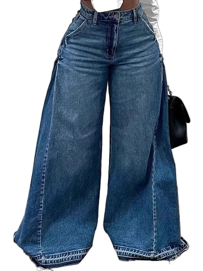 A person wearing very wide-leg blue denim jeans with a white cropped top and a small black handbag, standing against a light gray wall.