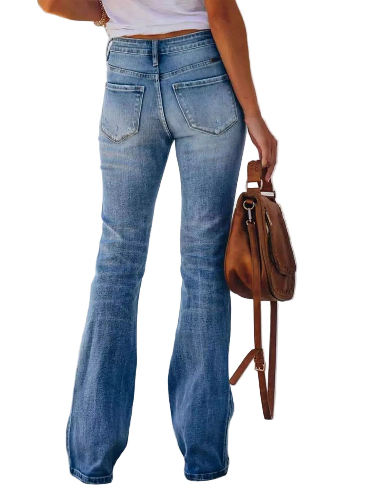 Person wearing blue jeans and holding a brown leather bag against a white wall.