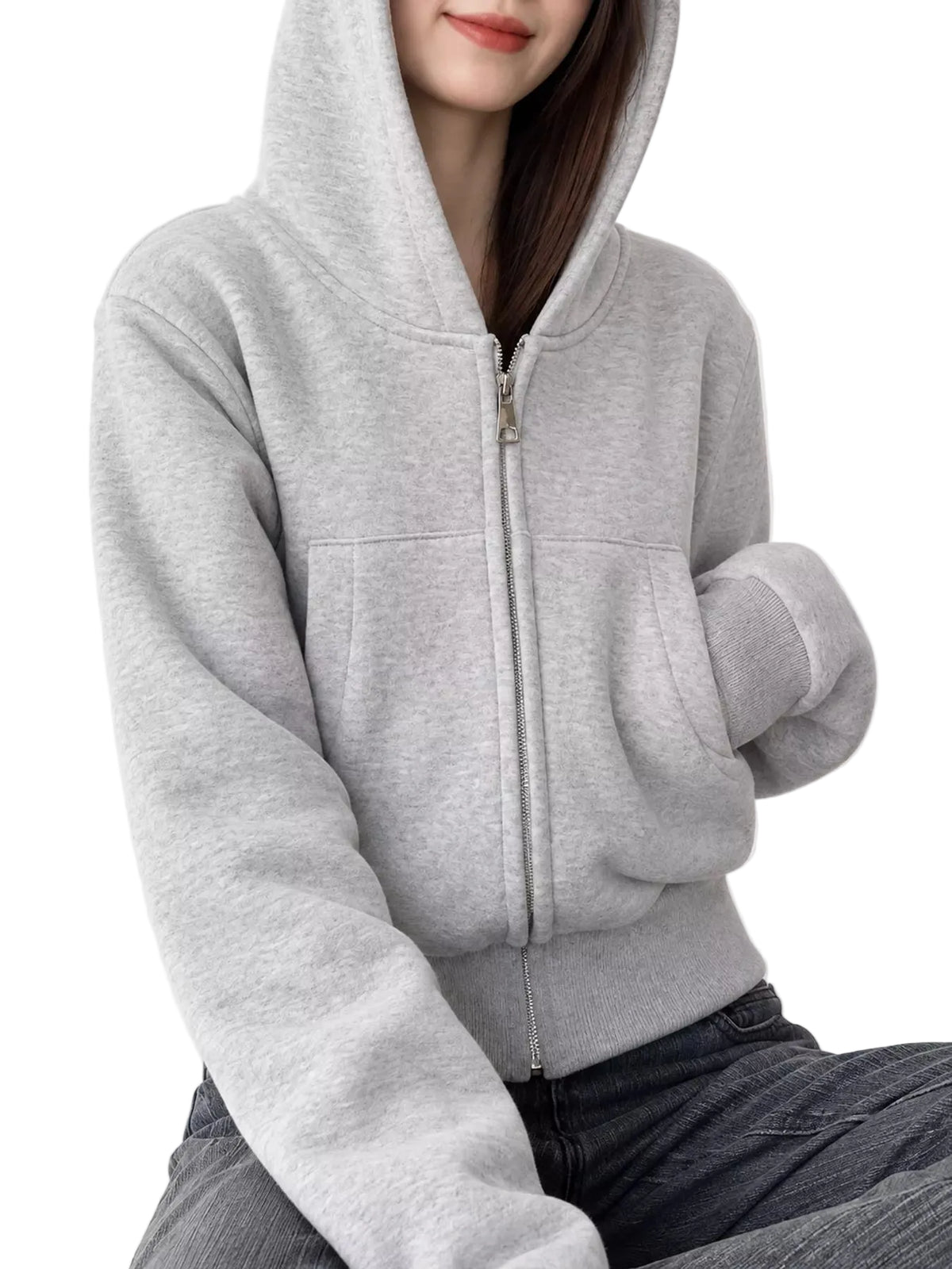 A woman wearing a light gray zip-up hoodie with a front zipper, kangaroo pockets, and ribbed cuffs and hem, paired with dark gray jeans against a plain light background.