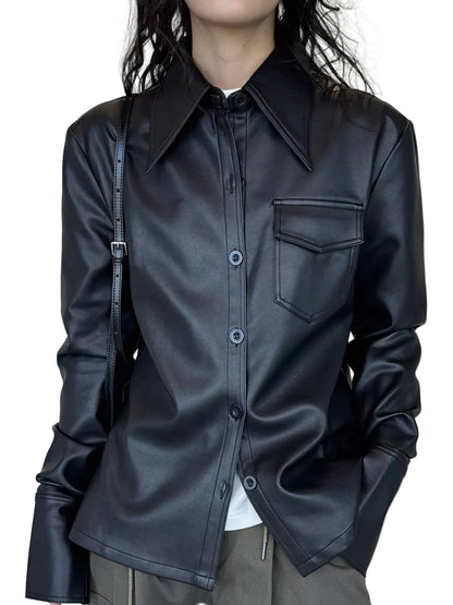 A person wearing a black faux-leather button-up shirt jacket with a pointed collar and a chest pocket, paired with gray pants and a black shoulder bag, set against a neutral cream curtain background.