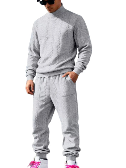 A man wearing a light gray knit two-piece sweatshirt and jogger pants set, standing in front of a white suburban house.
