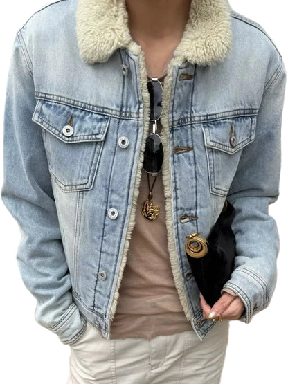 A person wearing a light-wash blue denim jacket with a cream sherpa collar, layered over a beige top and cream pants, holding a black clutch bag.