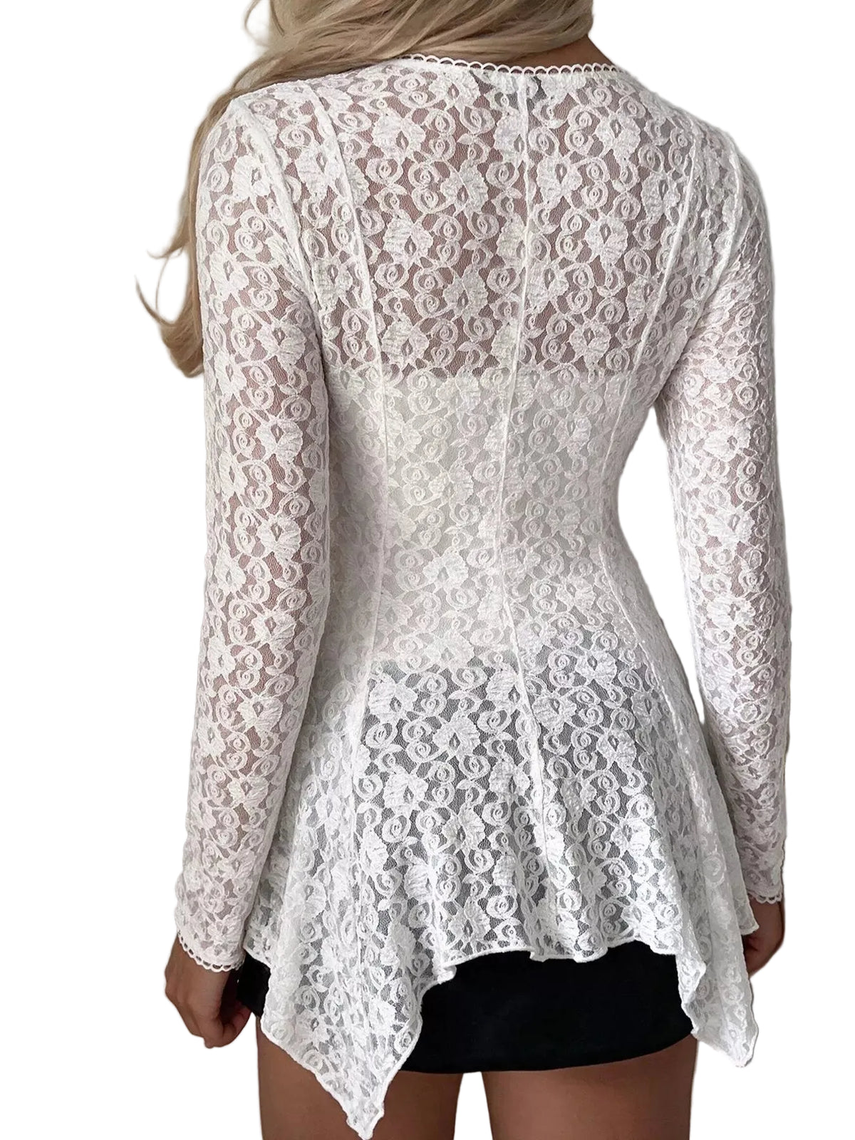 A woman shown from the back wearing a white lace long-sleeve top with a peplum hem over a black skirt, set against an indoor wall background.