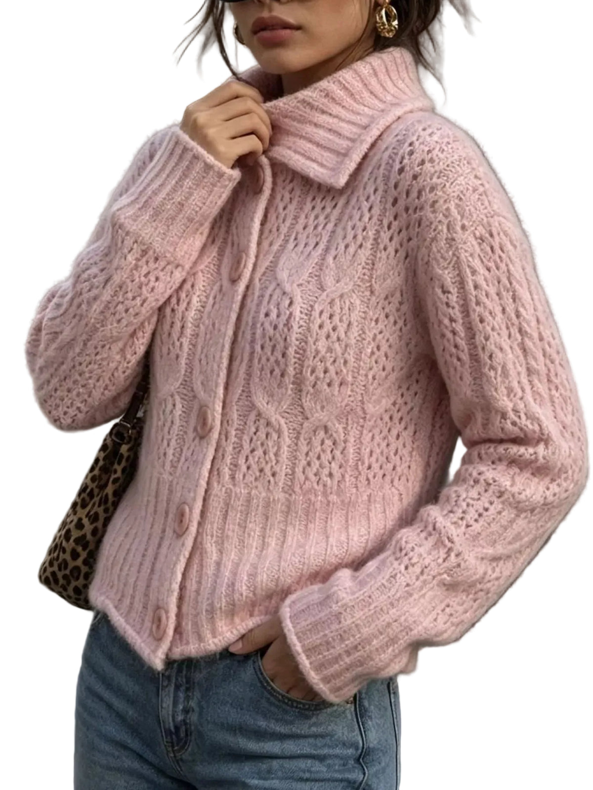 A woman wearing a light pink cable-knit button-up cardigan with a high collar, paired with blue jeans and a leopard-print shoulder bag, standing outdoors next to a dark gray pole.