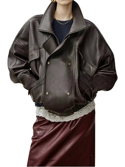A model wears an oversized dark brown leather jacket with a double-breasted snap closure, styled over a navy top and a burgundy leather skirt against a neutral studio background.