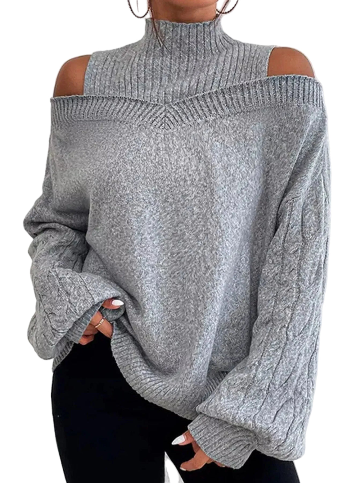 A person wearing a light gray ribbed knit sweater with cold-shoulder cutouts and a high mock neck, paired with black pants, standing against a white textured wall.