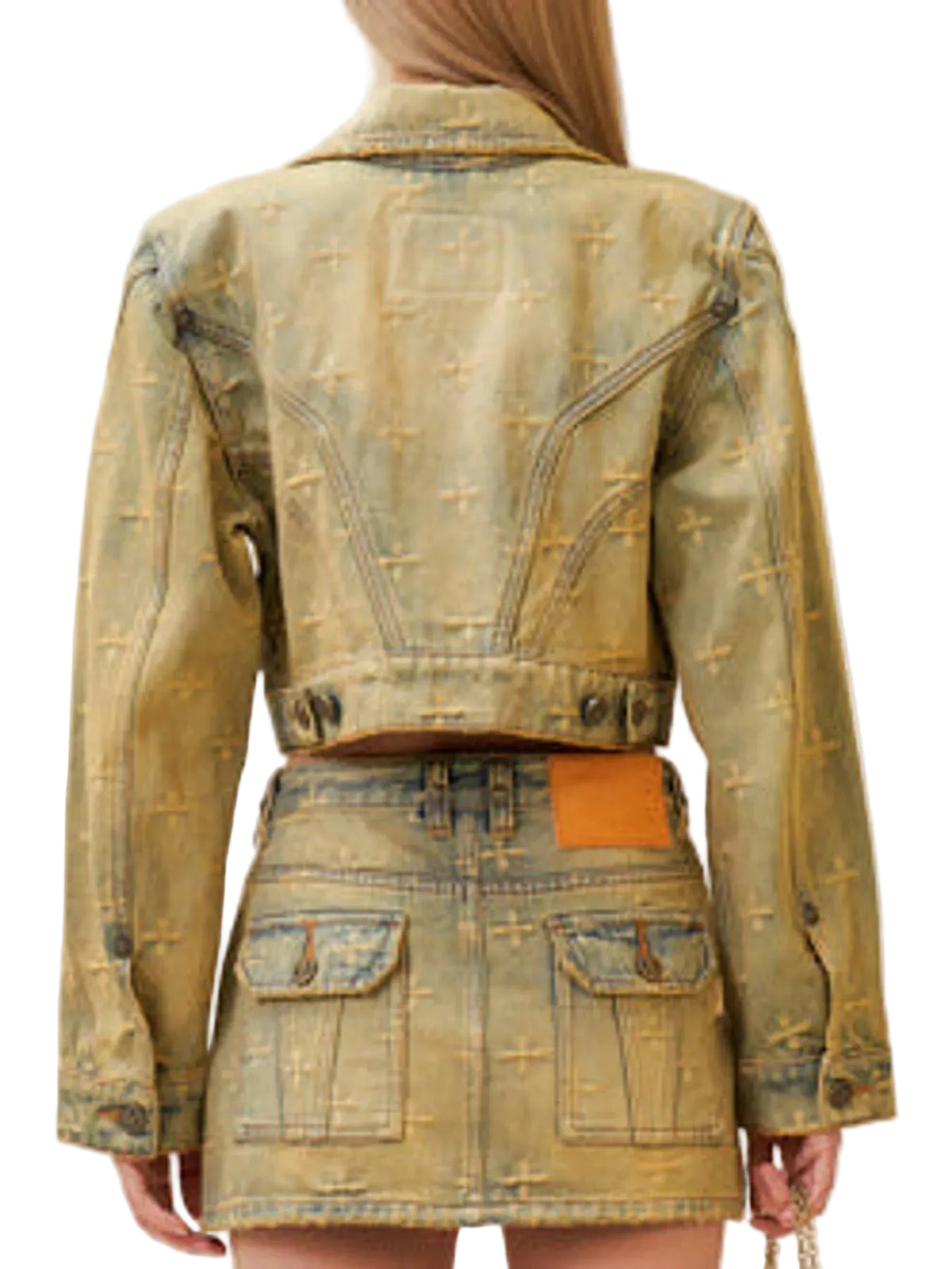 Back view of a model wearing a cropped, distressed denim jacket and matching denim mini skirt with a tan leather patch on the back waist.