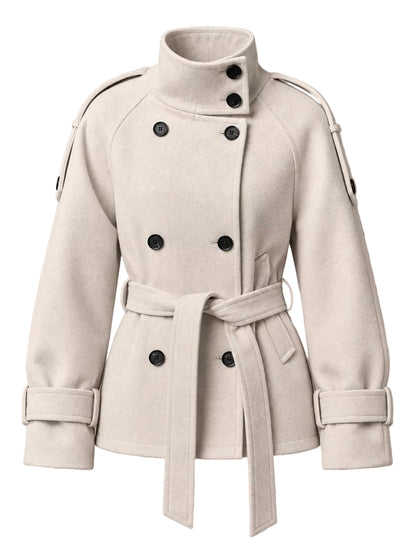 A cream-colored double-breasted coat with a high stand-up collar, matching waist belt, and dark buttons, shown against a solid taupe background.