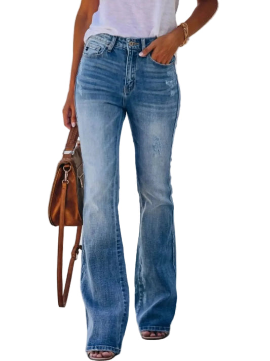 A person wearing light-wash blue flare jeans with a white top, holding a brown leather shoulder bag, standing against a white wall.