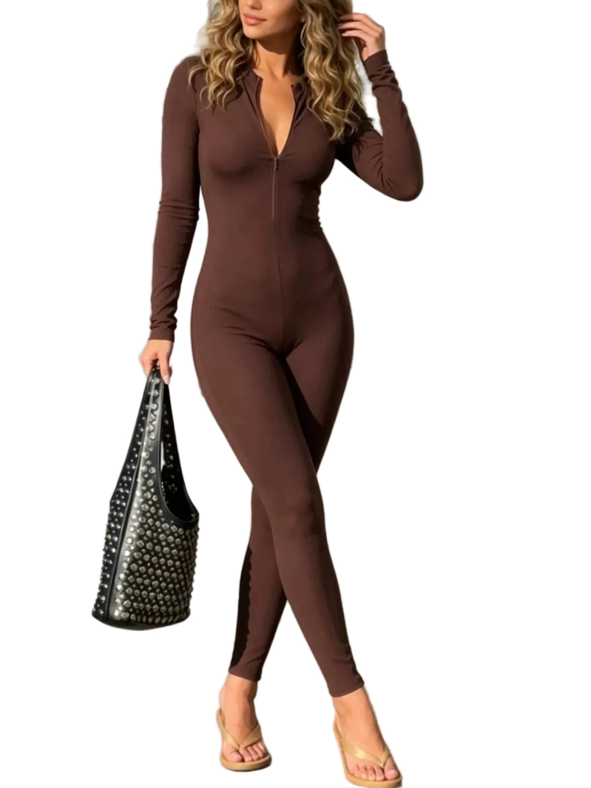 A woman wearing a brown long-sleeve zip-front bodysuit or jumpsuit walks on a sidewalk, holding a black studded handbag. The setting is outdoors near white columns and a building entrance.