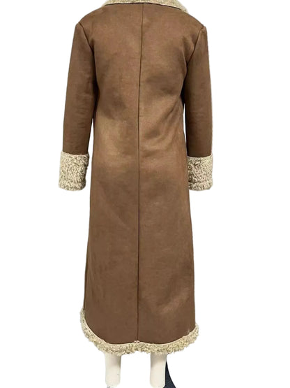 A long brown faux-suede coat shown from the back on a mannequin, featuring cream-colored textured trim at the collar, cuffs, and hem, set against a window with horizontal blinds.