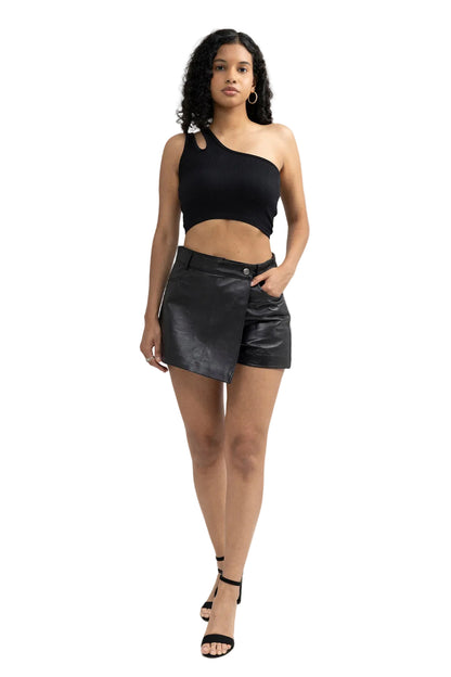 Woman wearing a black one-shoulder top and leather shorts on a white background