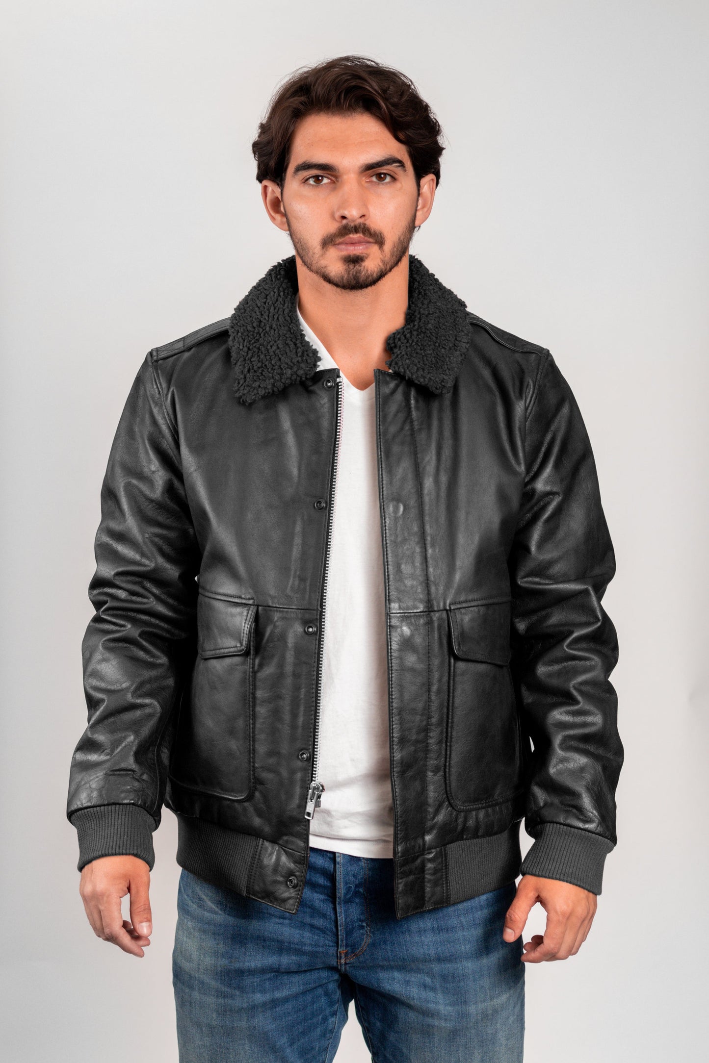 Man wearing a black leather jacket with a white shirt and blue jeans on a gray background
