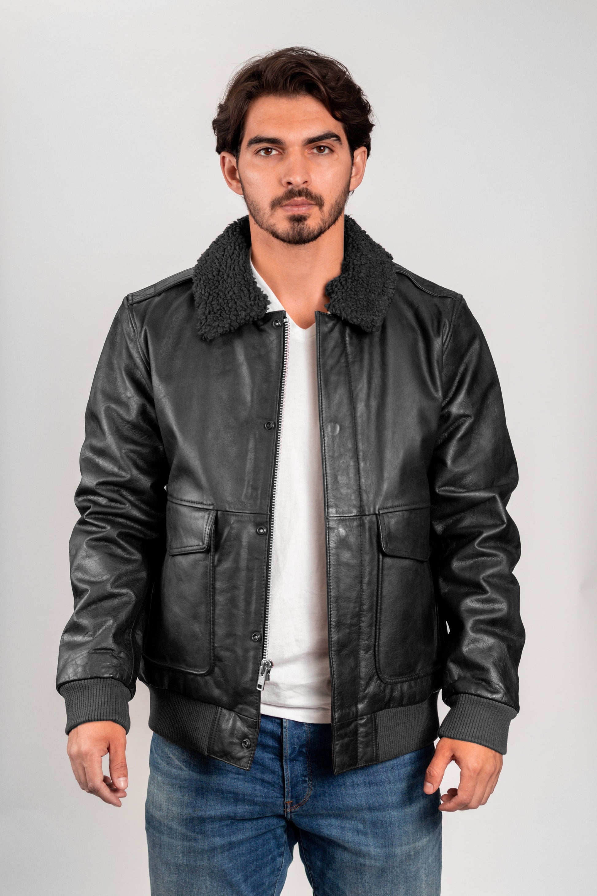 Man wearing a black leather jacket with a white shirt and blue jeans on a gray background