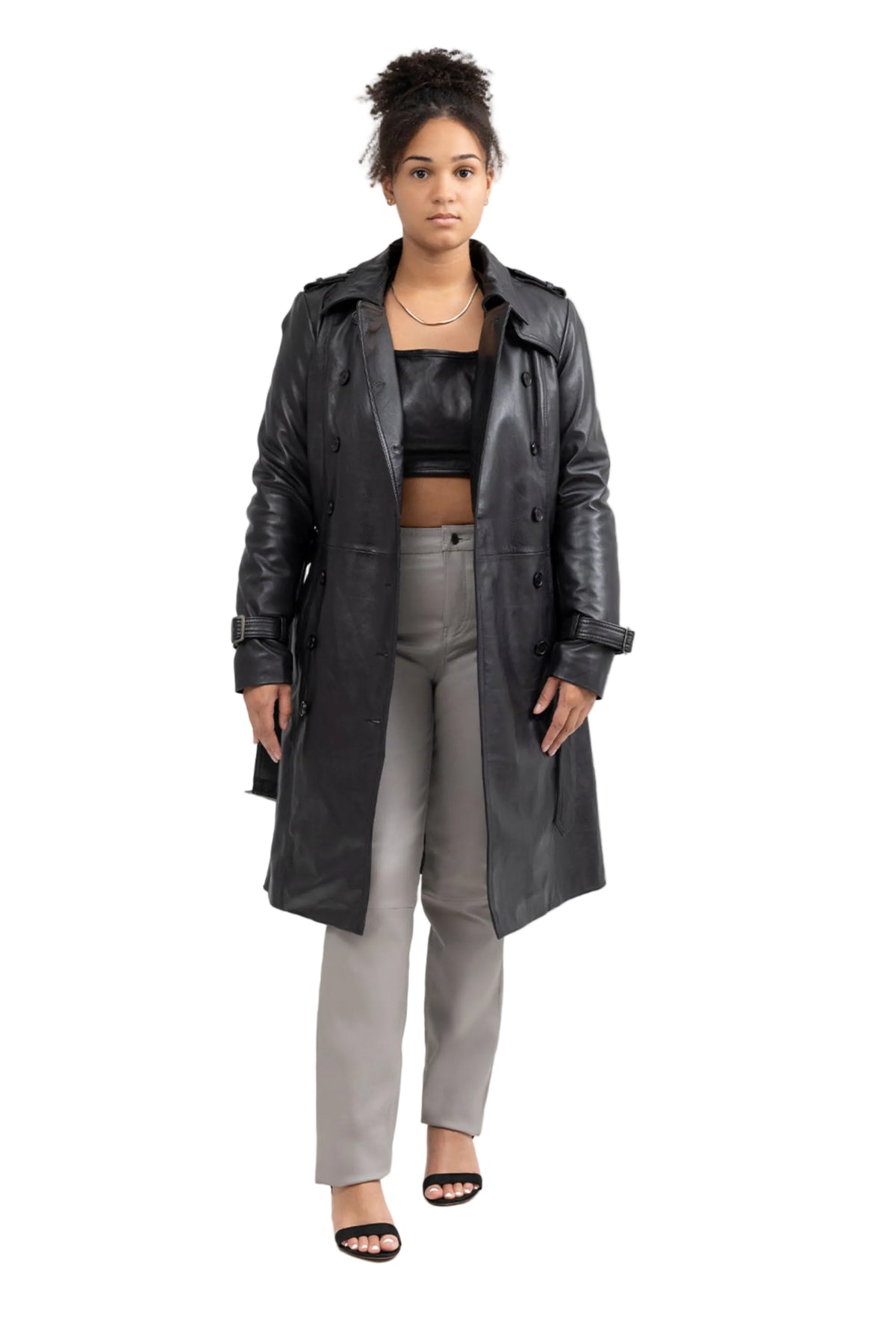 Woman wearing a long black coat over a black top and gray pants on a white background