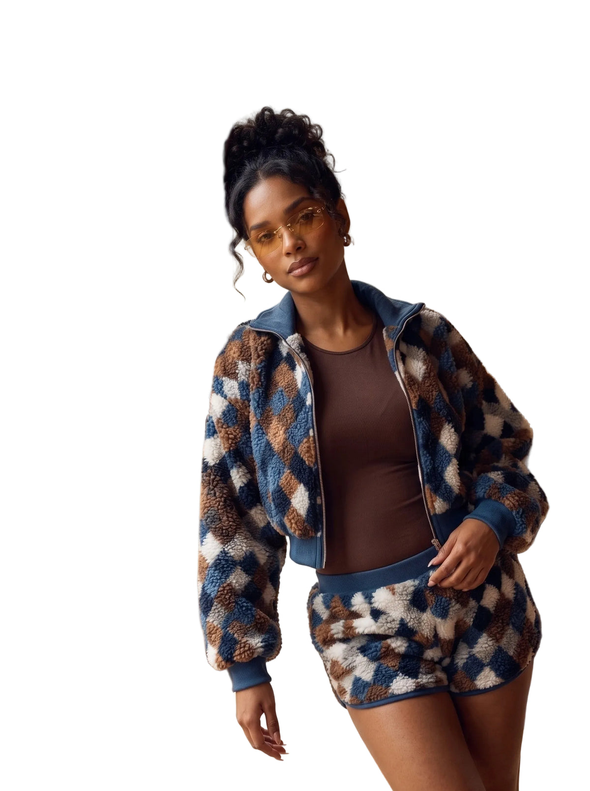A woman wearing a matching fuzzy zip-up jacket and shorts set in a blue, brown, and cream diamond pattern, standing by a large window in a wooden cabin.
