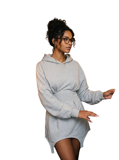 A woman wearing a light gray oversized hoodie dress stands in a cozy book and vinyl record store, reaching for records on a shelf.