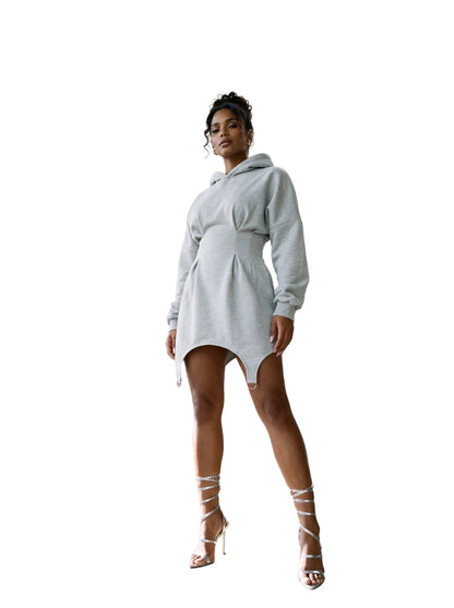 A woman models a light gray oversized mini hoodie dress in a modern concrete architectural setting with curved walkways and columns.